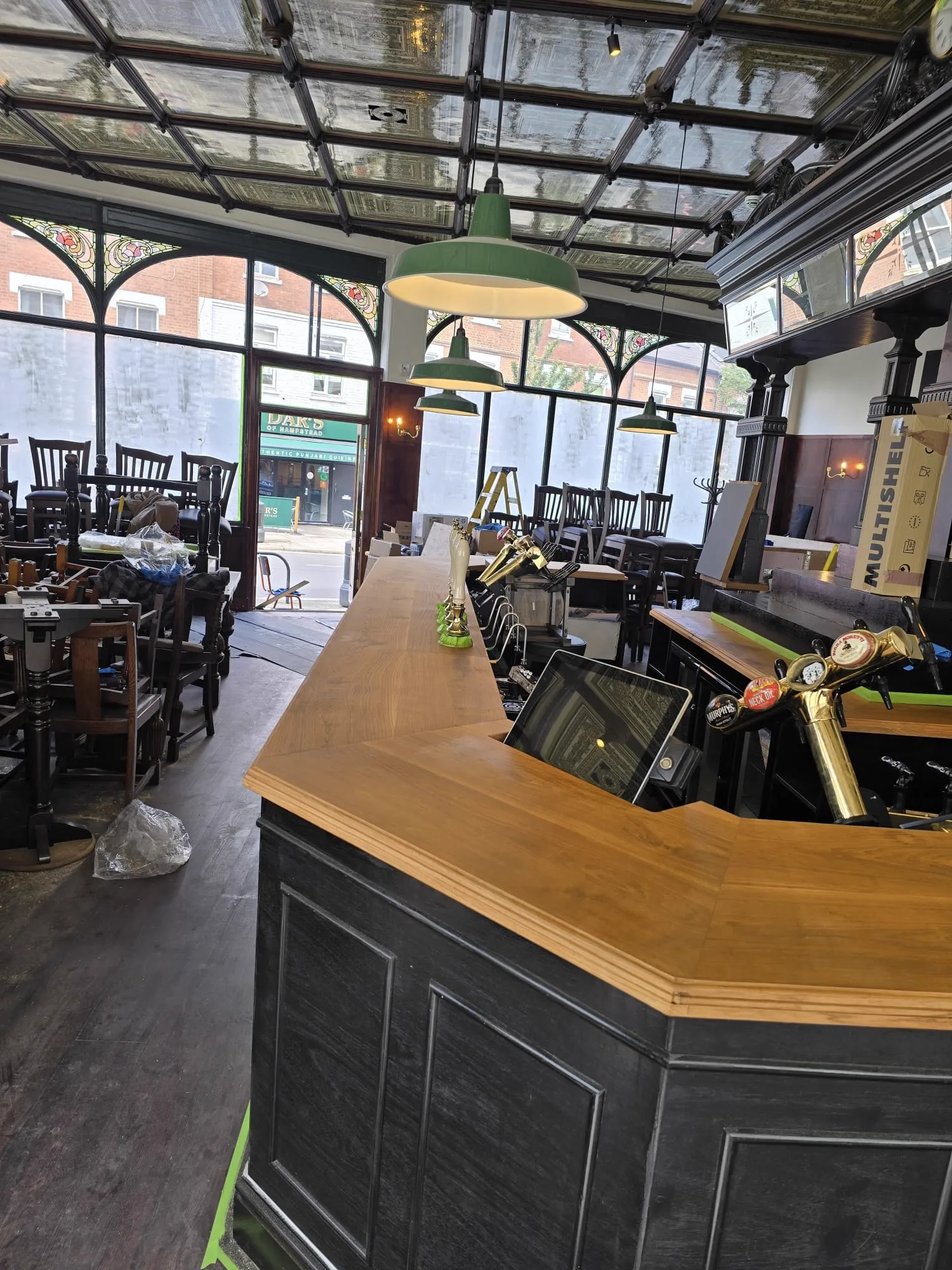 Oak bar counter in the final stages with green pendant lights, brass taps and stacked chairs